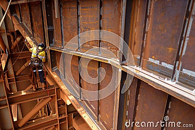 Side view of abseiler rope access repairer hanging in fall restraint position performing oxy acetylene cutting metal beam Stock Photo