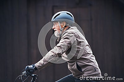 Active senior man with bike helmet cycling outdoors againts dark background. Stock Photo