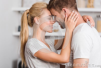 side view of affectionate couple hugging in kitchen and touching Stock Photo