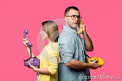 side view of angry young couple standing back to back and talking by rotary phones isolated Stock Photo