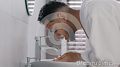 Side view arab spaniard indian arab man guy opens faucet near washbasin at home in hotel bathroom washes face with hot Stock Photo