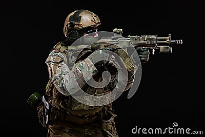 Side view of army man dressed in camouflage and full military equipment, wearing helmet, glasses and protective mask Stock Photo