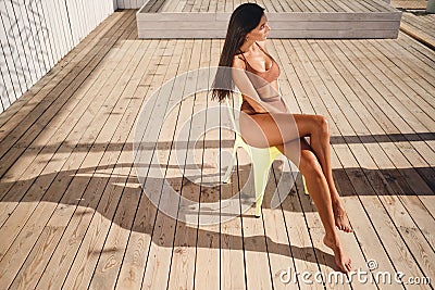 Side view of attractive brunette girl in swimsuit dreamily sunbathing on chair on beach Stock Photo