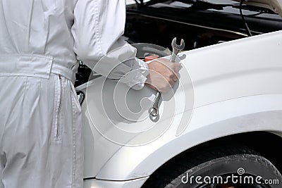 Side view of automotive mechanic in uniform with wrench diagnosing engine under hood of car at the repair garage. Stock Photo