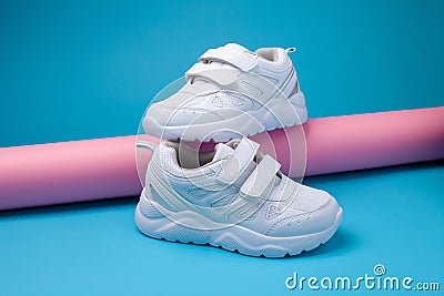 side view balance of two white unisex sneakers on a pink long paper roll on a blue background, one sneaker stands on the Stock Photo