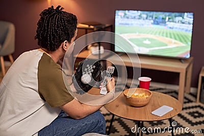 Side view baseball fan holding TV remote while watching match at home Stock Photo