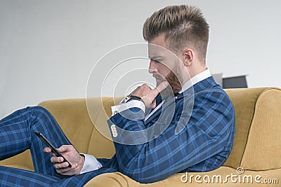 Side view of beautiful sexy businessman sitting on a sofa in a suit and using his phone Stock Photo