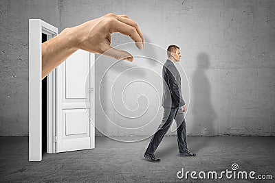 Side view of big man`s hand emerging from the dark on white doorway and ready to grab little businessman who is walking Stock Photo