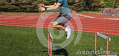 Side view of a boy jumping over a track hurdle Stock Photo