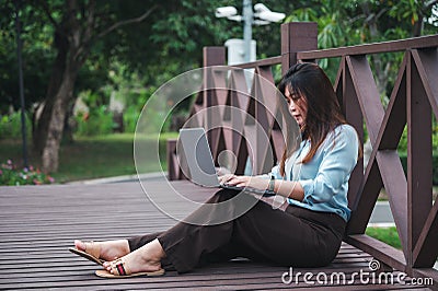 A side view of a brown-haired woman sitting on a wooden bridge in a park using a laptop computer. A young office worker talking on Stock Photo