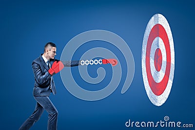 Side view of businessman wearing red boxing gloves and holding out one hand towards big round target. Stock Photo