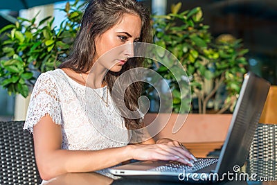 Side view of busy young female freelancer thinking over the project and working on her laptop at sidewalk cafe Stock Photo