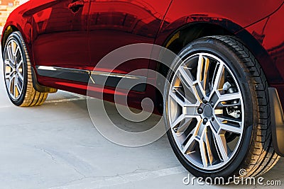 Side view of a car. Tire and alloy wheel of a modern red car on the ground at the sunset. Car exterior details. Stock Photo
