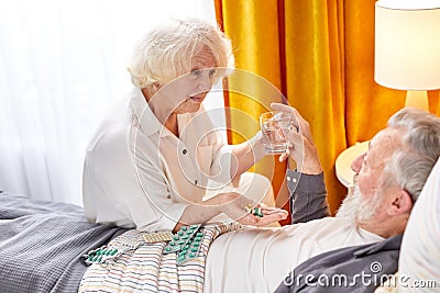 side view on careful mature woman giving pills and cup of water to sick husband Stock Photo