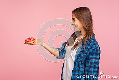Side view of cheerful pretty girl in checkered shirt giving delicious donut and smiling, offering quick high-calorie snack Stock Photo