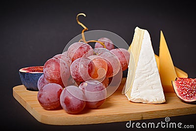 Side view of Cheeseboard platter with hard and soft mould cheese, grape and segmented fig on wooden board Stock Photo