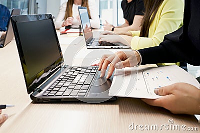 Side view of crop female working on laptop and taking notes on paper while sitting at table with group of colleagues in Stock Photo