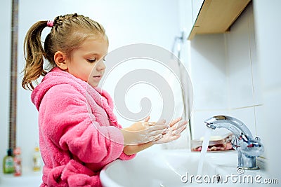 Side view of cute little girl with ponytail in pink bathrobe washing her hands. Stock Photo