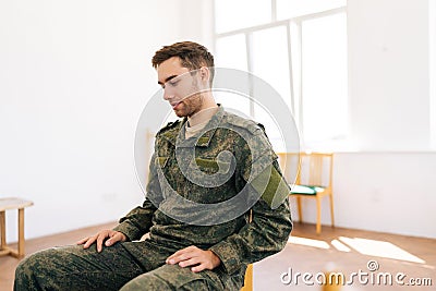 Side view of depressed Caucasian male veteran in camouflage uniform talking about trauma in PTSD support group. Concept Stock Photo