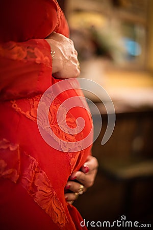 Side view of Detail of pregnant woman with red dress with hands on belly Stock Photo