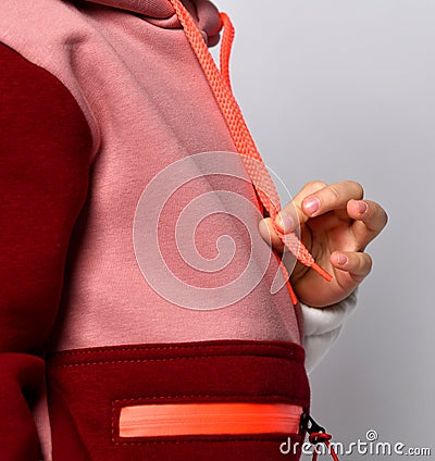 Side view detail of stylish girl sport coat colored in red, pink and white. Hand of model holding hoodie string. Stock Photo