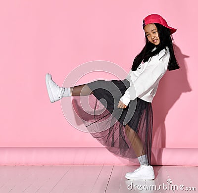 Side view of a little Korean girl model posing in the studio on a pink background raising her leg. Stock Photo