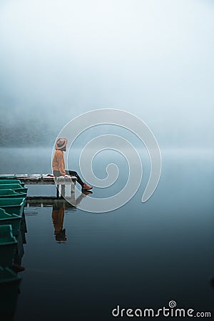 Side view of fashioned young woman sitting on wooden dock looking at view on a misty morning Stock Photo