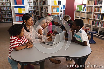 Female teacher teaching schoolkids on laptop at table in school library Stock Photo
