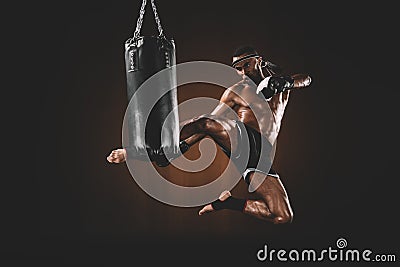 Side view of focused muay thai fighter practicing kick on punching bag Stock Photo