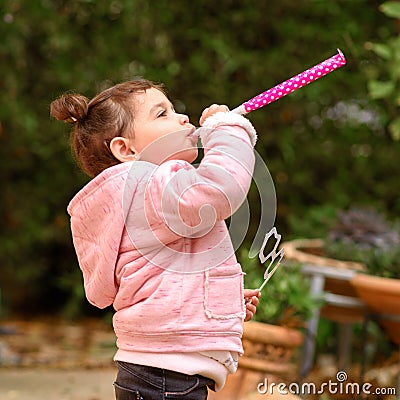 Side view of funny little girl celebrating, blowing in pipes. Birthday outdoor party, Purim. Stock Photo
