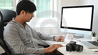 Side view of graphic designer or photographer is sitting in front of empty screen computer and taking notes. Stock Photo