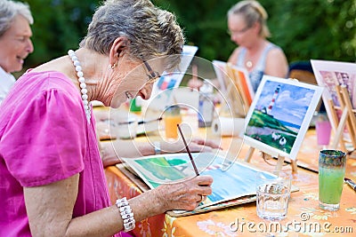 Side view of a happy senior woman smiling while drawing as a recreational activity or therapy outdoors together with the group. Stock Photo