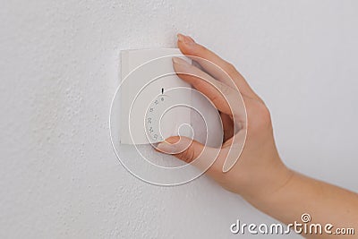 Side view of human hand turns off the heating at home. Central Heating thermostat control dial adjustment Stock Photo