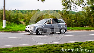 Side view KIA Rio car second generation moving on rural asphalt road. Driver with passenger in old silver color hatchback riding Editorial Stock Photo