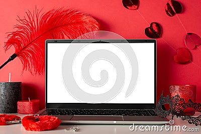 Side view of laptop, candles, mask, and adult toys furry handcuffs and feather tickler on red background Stock Photo