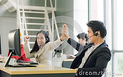 Side view of line of call center employees are smiling and working on computers. Two of them are shaking hands Stock Photo