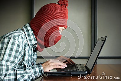 Side view of masked hacker wearing a balaclava looking a laptop and stealing important information data. Network security and priv Stock Photo