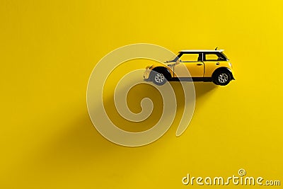 Side view of a Mini Cooper S Yellow toy car on a yellow background with a long shadow Stock Photo