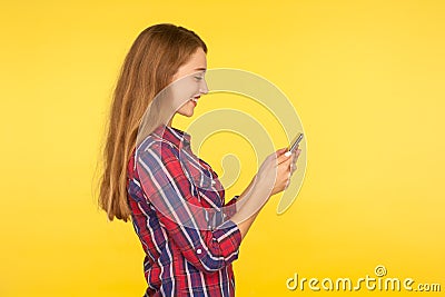 Side view of mobile customer smiling, happy girl in shirt typing message on smartphone, looking satisfied pleased with app Stock Photo