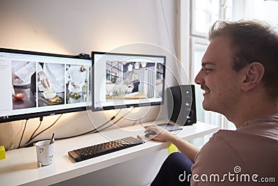 Side view, one young mans head looking at two monitors in front of him. in his room. keyboard, mouse and speakers visible at desk Stock Photo