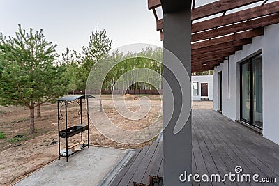 Side view of an open veranda in front of a modern forest cottage. Pine young forest under the sunset rays in the Stock Photo