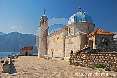 Side view of Our Lady of the Rocks islet off the coast of small old town Perast in Bay of Kotor, Montenegro mountainous background Stock Photo