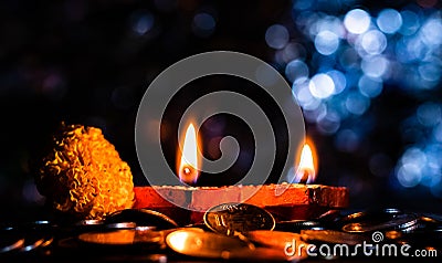 Side view of a pair of glowing Terracotta lamps with flower and coins, and blue colored bokeh in the background. Prosperity Stock Photo
