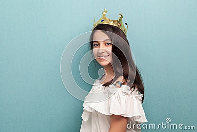 Side view portrait of beautiful little princess wear in white dress and golden diadem crown standing, looking at camera with Stock Photo