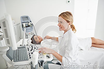 Young doctor using ultrasound scanner and examining thyroid of young lady Stock Photo