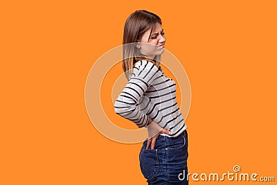 Side view portrait of sick woman with brown hair in long sleeve striped shirt standing with grimace of pain. indoor studio shot Stock Photo