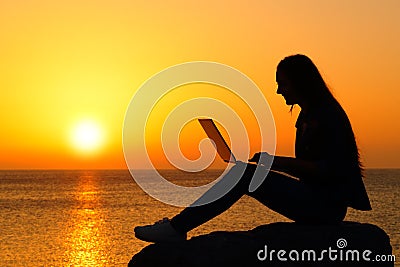 Silhouette of a woman using laptop at sunset Stock Photo