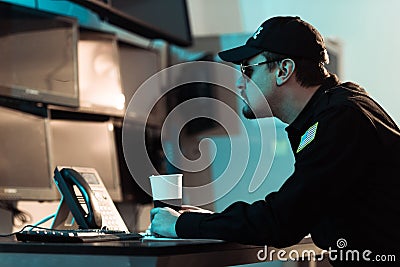 side view of prison guard sitting with cup of coffee and monitoring people Stock Photo