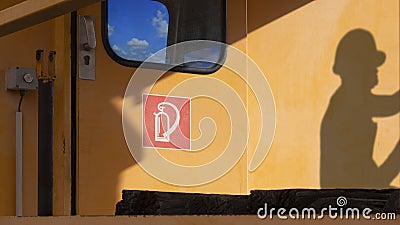 Side view of red fire extinguisher sign on train head door with sunlight and shadow of engineer on surface of orange train wall Stock Photo