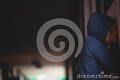 Side view of sad boy covering his face with hands while leaning on wall Stock Photo